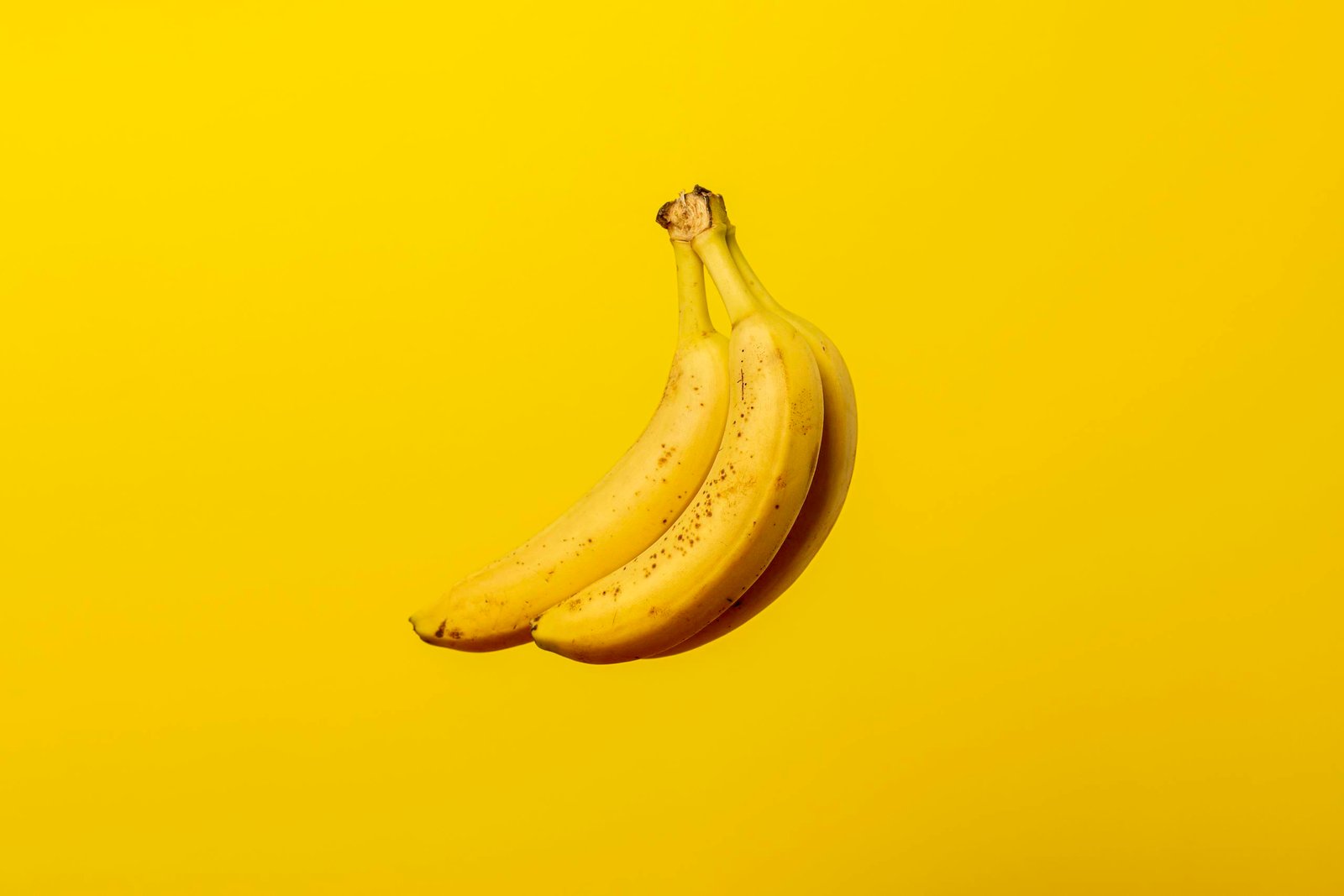 A bunch of ripe yellow bananas against a vivid yellow backdrop, offering tropical freshness.