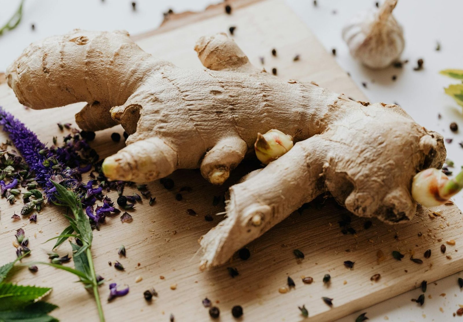 Close-up of fresh ginger root surrounded by spices and herbs on a wooden chopping board.