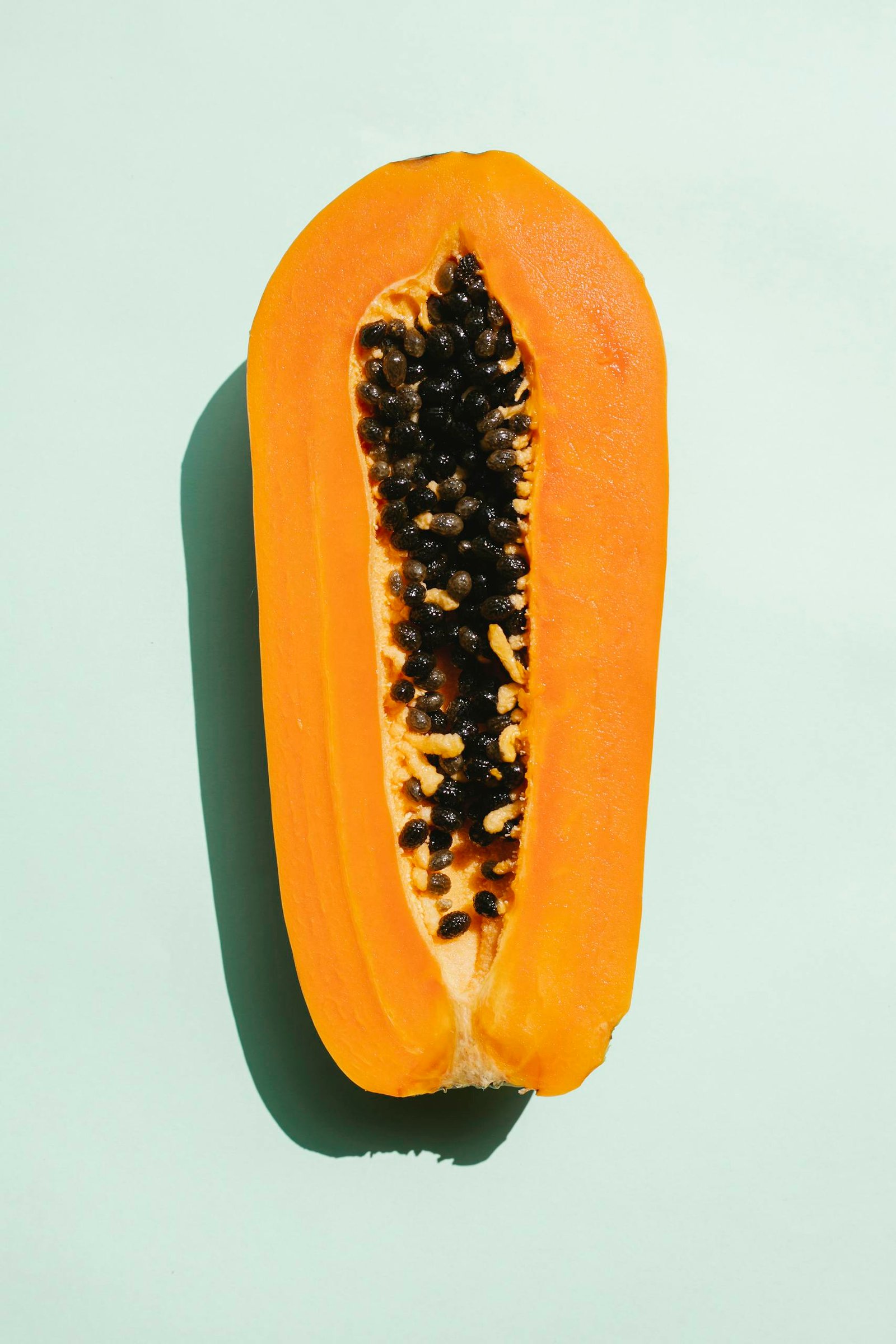 Bright halved ripe papaya on a light mint background, showcasing its vibrant seeds.