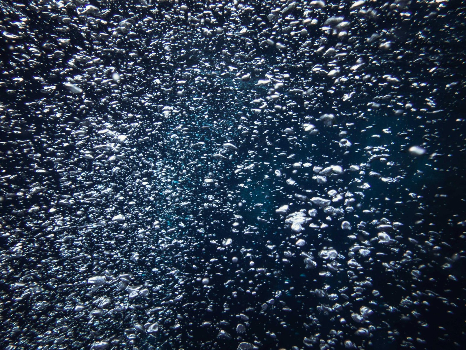 Captivating view of countless bubbles rising underwater against a deep blue background.