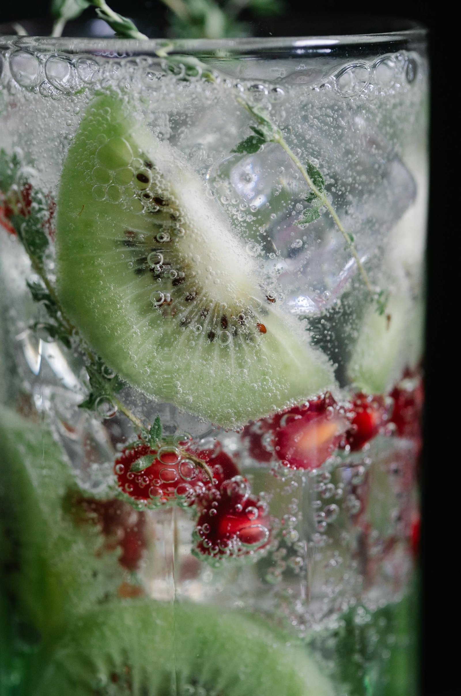 Close-up of a refreshing drink with kiwi slices, pomegranate seeds, and ice cubes.