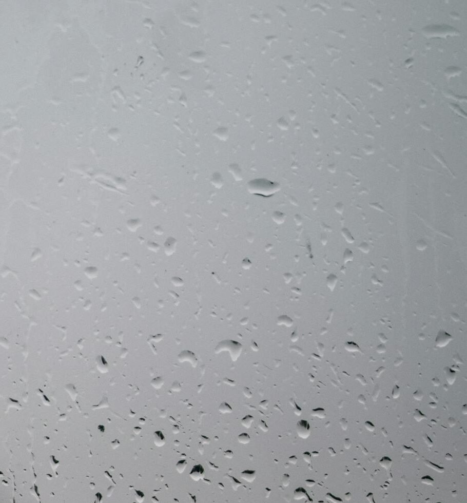 Close-up of raindrops on a window with a blurred view of the outdoors, creating a moody ambiance.