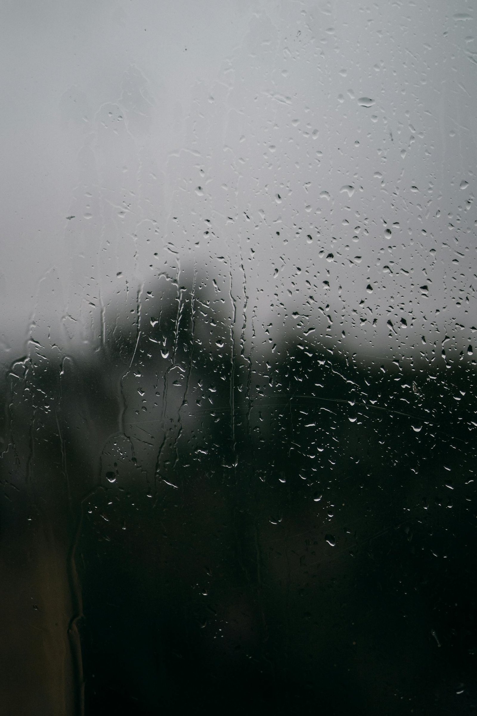 Close-up of raindrops on a window with a blurred view of the outdoors, creating a moody ambiance.
