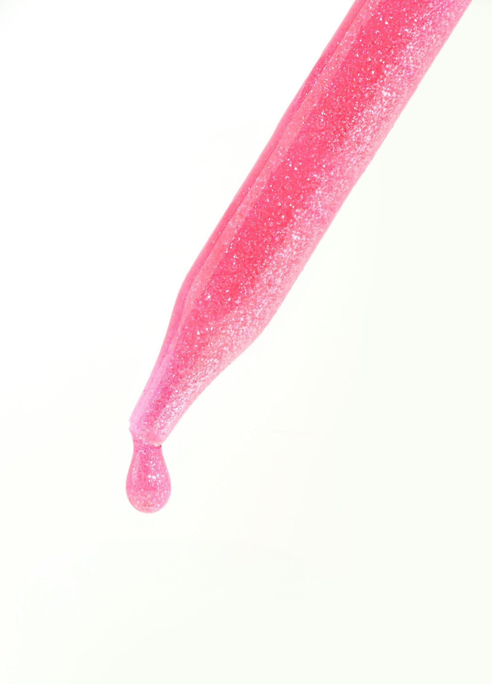 Close-up of a pink glitter dropper releasing a single shimmering liquid drop against a white background.
