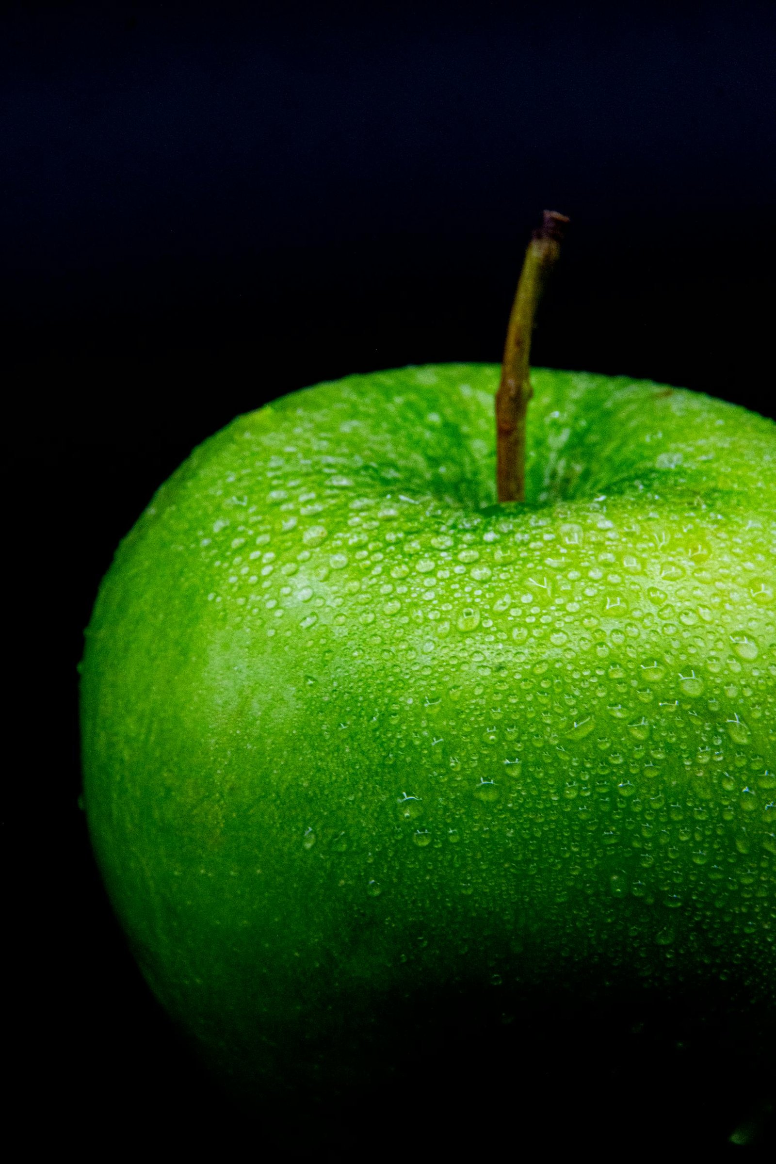 Macro shot of a fresh green apple with water droplets against a dark background.
